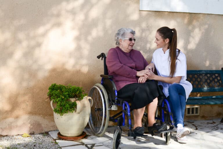 Elderly senior woman on wheelchair with nurse outdoor nursing home